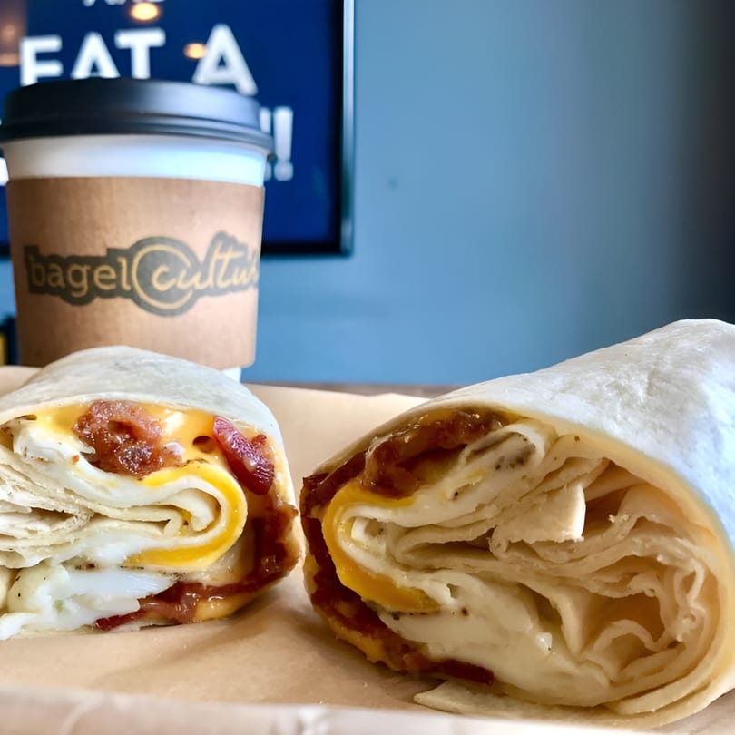 Two breakfast wraps with egg, cheese, and bacon, next to a Bagel Culture coffee cup.