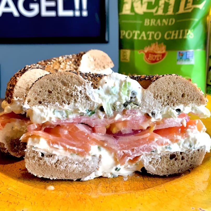 Everything bagel with lox, cream cheese, and tomato, served with a bag of chips.