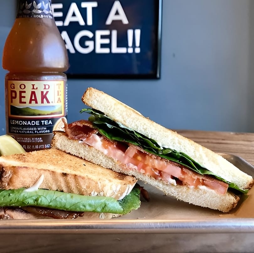 Two halves of a BLT sandwich on a metal tray with a bottle of Gold Peak Lemonade Tea.