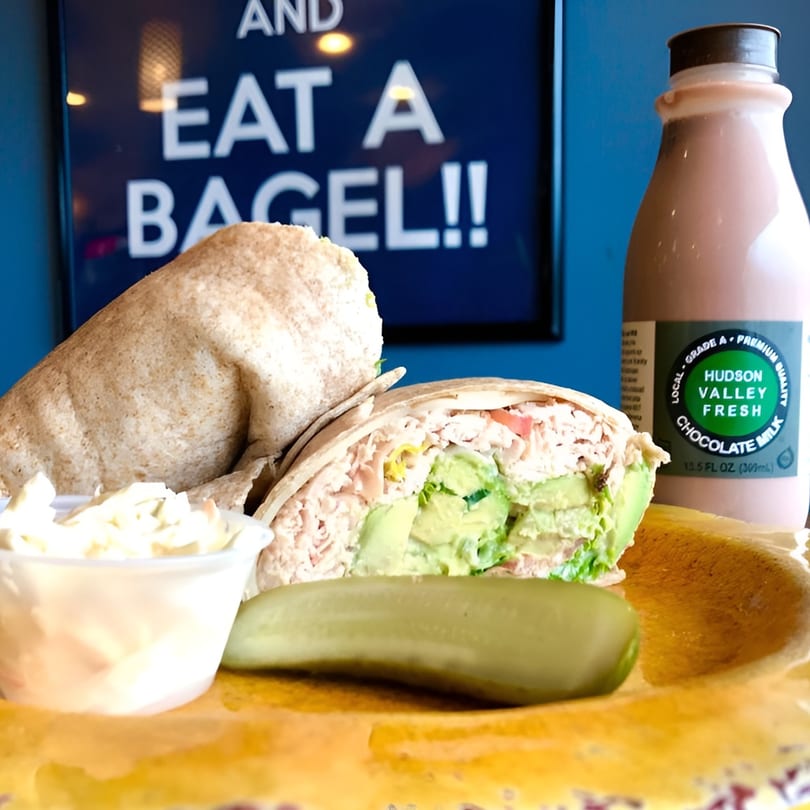 A chicken and avocado wrap, coleslaw, pickle, and chocolate milk on a yellow plate.