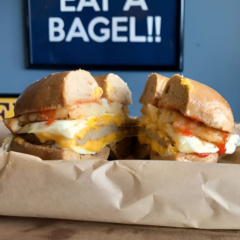 A Bagel Culture breakfast sandwich, cut in half, with egg, cheese, sausage, and hash browns.