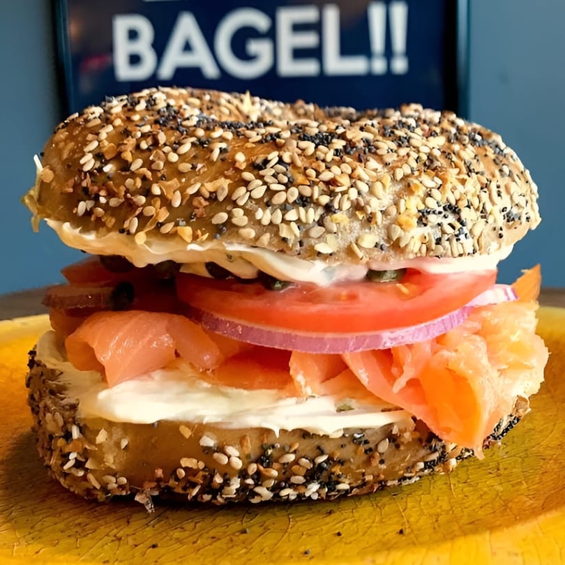 Everything bagel with lox, cream cheese, tomato, red onion, and capers on a yellow plate.